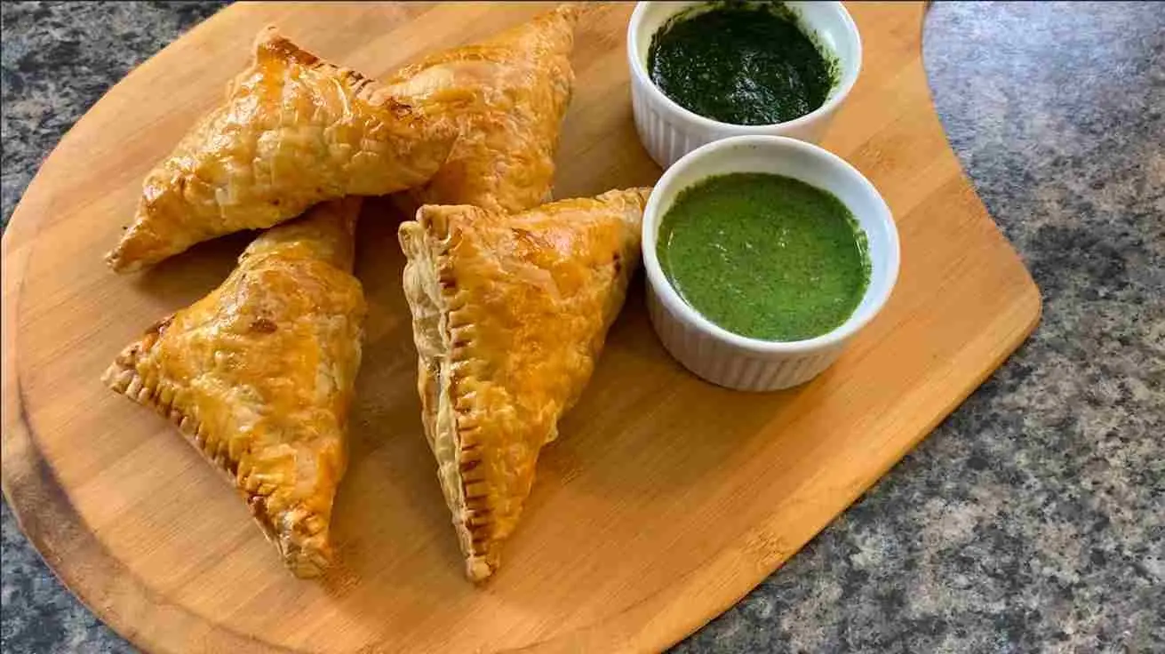 Baked patties on a wooden board beside two bowls of green chutney