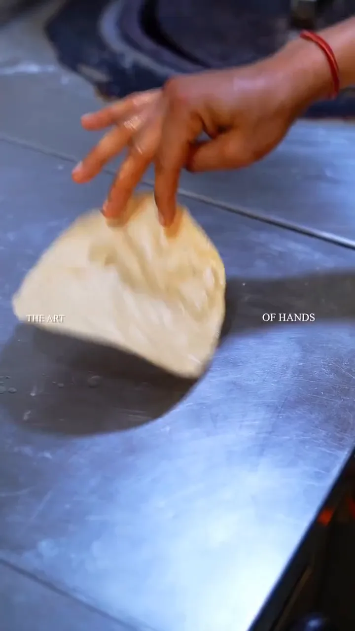 Hands stretching dough on a steel kitchen counter